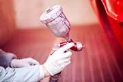 Worker painting a red car in paiting booth using professional tools and spray gun