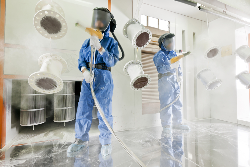 Worker wearing protective wear performing powder coating of metal details in a special industrial products